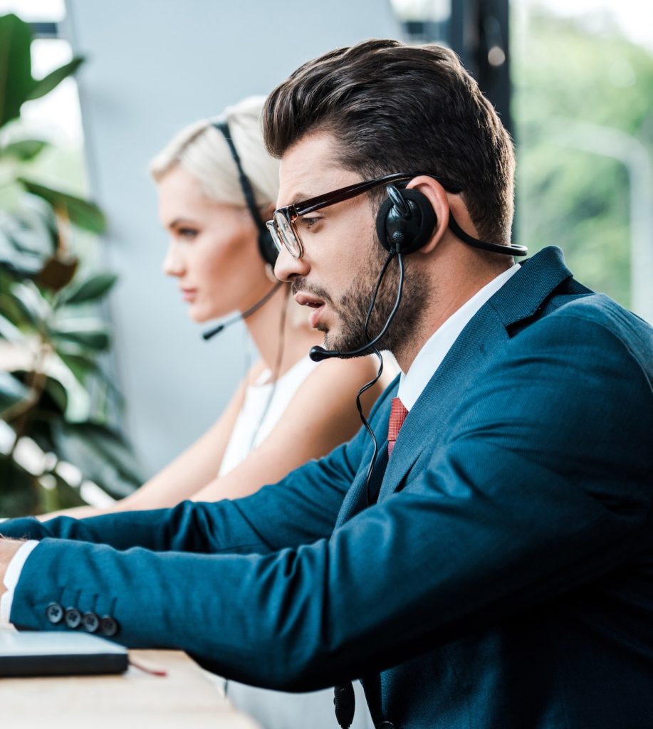 selective focus of handsome man in headset typing on laptop while working near colleague